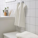 Witte FREDRIKSJÖN handdoeken hangen netjes aan het wandrek, naast tandenborstels en plant.
