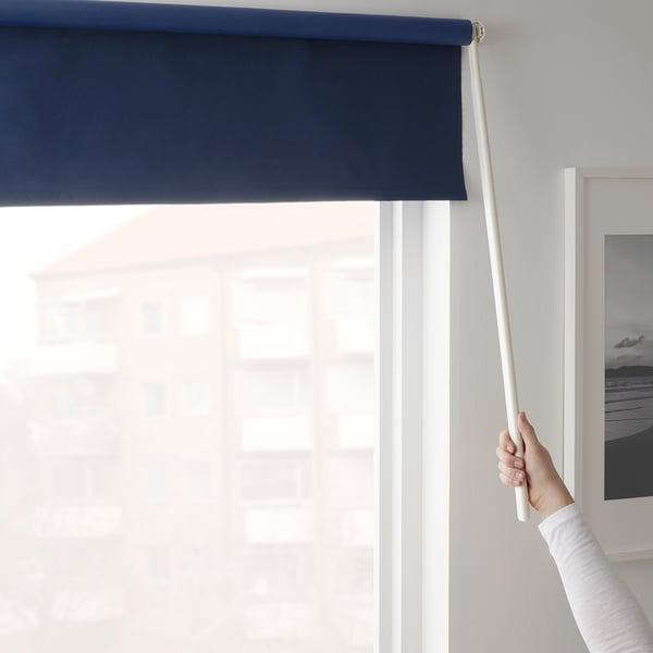Een hand steekt een toverstok op om een blauw rolgordijn te bedienen en het licht te blokkeren.
