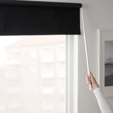 Een hand die een zwart rolgordijn opheft met een witte toverstok, die licht blokkeert.