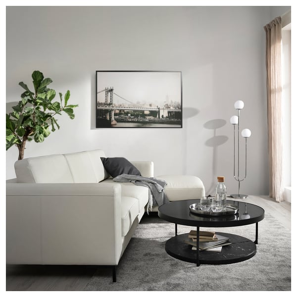 Moderne woonkamer met witte sectionele, grijze vloerkleed, zwarte salontafel, stadskunst, lamp, plant.