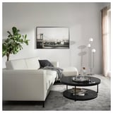 Moderne woonkamer met witte sectionele, grijze vloerkleed, zwarte salontafel, stadskunst, lamp, plant.