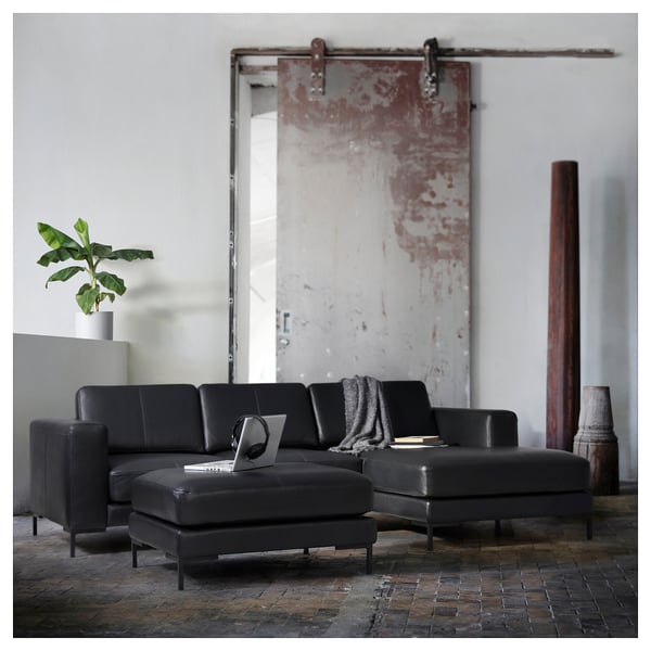 Moderne woonkamer met zwarte lederen bank, schuifdeur, plant, laptop.