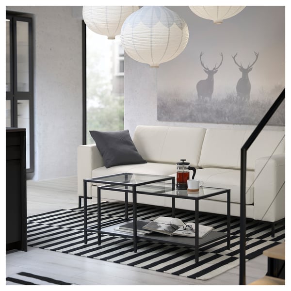 Moderne woonkamer met wit lederen FULLERÖ bank, zwart-wit gestreept tapijt, glazen salontafel en kunst aan de muur van hertensilhouetten.