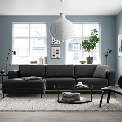 Moderne woonkamer met zwarte FULLERÖ bank, grote ramen, grijze muren, witte hanglamp en ronde salontafel.
