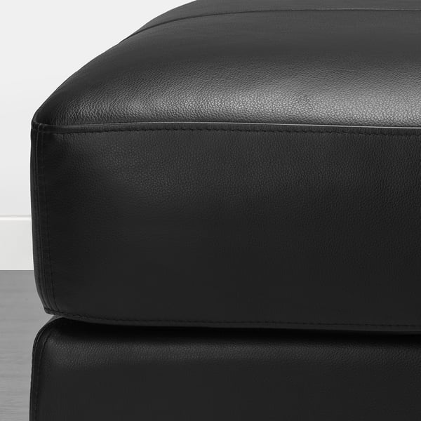 Close-up van zwart lederen sofa voetenbank, met glad, hoogwaardig generfd leer met zichtbare stiksels en strakke randen.