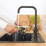 Persoon die groenten wast in de gootsteen met GAMLESJÖN-kraan, wat water en energie bespaart.