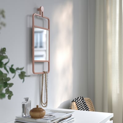 Een aan de muur gemonteerde spiegel met een koperen frame en een plank eronder, met daarin een ketting en een fles.