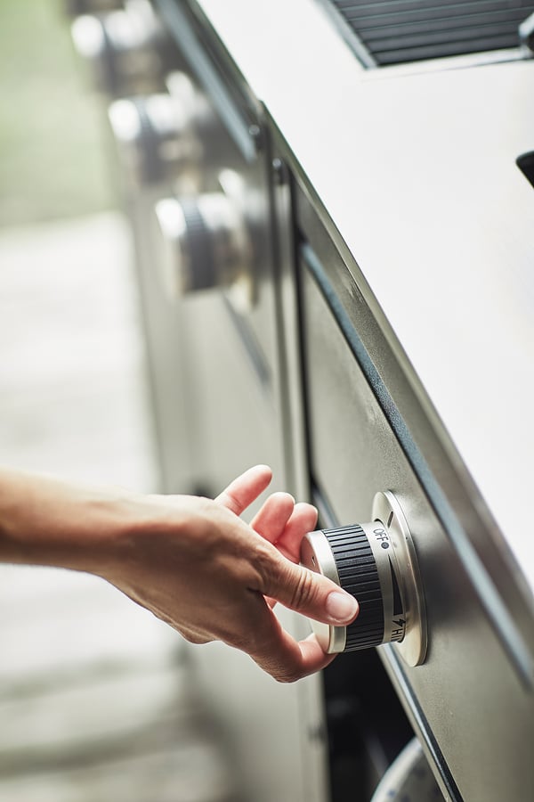 Hand draait zilveren knoppen op metalen kookplaat, waarschijnlijk een GRILLSKÄR-grill in de keuken.