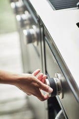 Hand draait zilveren knoppen op metalen kookplaat, waarschijnlijk een GRILLSKÄR-grill in de keuken.