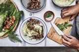 Chef-kok die maaltijd bereidt met verse champignons, venkel en kruiden. Plaat van voedsel, snijplank met mes, kommen en groenten.