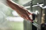 Persoon die een groene gasgrill voor buiten met roestvrijstalen bedieningselementen aanpast.