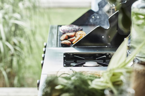 Zilveren grill in gebruik, voedsel buiten koken met groen op de achtergrond.