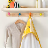 Kinderhanddoek met bijenmotief hangt aan de haak; houten plank met speelgoed erboven.