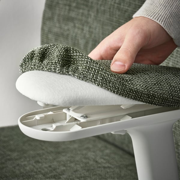 Een hand tilt een wit, verstelbaar lendensteunkussen op van een groene bureaustoel en toont de ergonomische ondersteuningsfunctie.