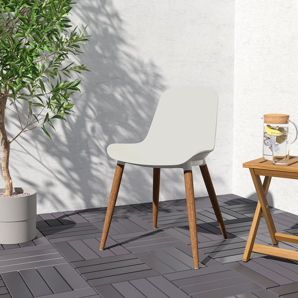 Witte GRÖNSTA stoel met houten poten, ontworpen voor comfort en eenvoudige reiniging, buiten bij een tafel met een waterkan en een potplant.