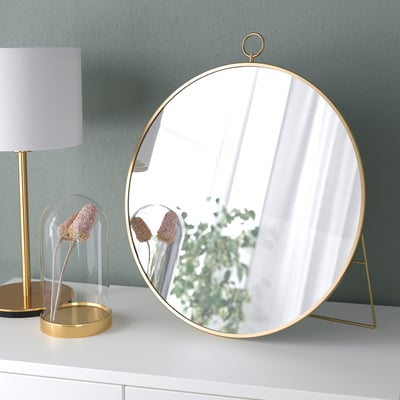Ronde spiegel met gouden lijst op standaard; hangt of staat; reflecterend oppervlak.