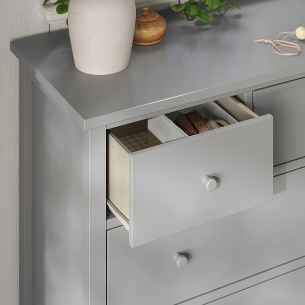 Grijze ladekast met een open lade die gecompartimenteerde items onthult. Blad gedecoreerd met vazen en planten.