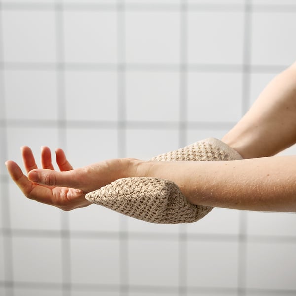 De persoon gebruikt de GULVIAL-scrubber op zijn hand en demonstreert zijn exfoliërende vingers tegen een betegelde muur.