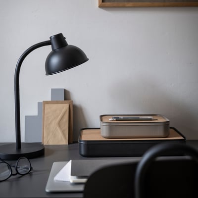 Zwarte bureauopstelling met HARVMATTA organizer. Metalen doos met kurkdeksel tussen lamp en glazen.