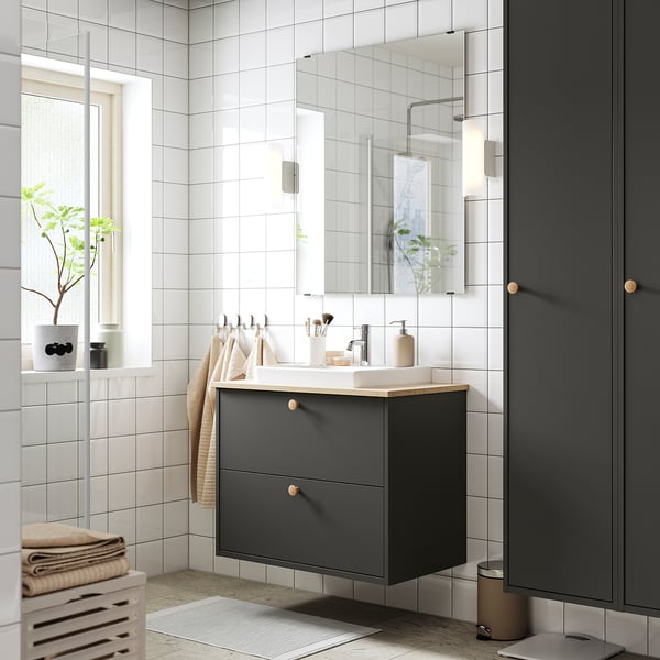 Moderne grijze badkamer met aan de muur gemonteerde wastafelkast. Witte gootsteen, chromen armaturen, spiegel en planten.