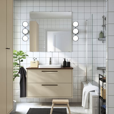Moderne beige badkamermeubel met strak design, ronde spiegel, planten en minimalistische inrichting.