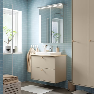 Moderne badkamer met blauw betegelde wanden, lichtbeige HAVBÄCK wastafelmeubel en wastafel, spiegelkast boven, handdoeken en planten.