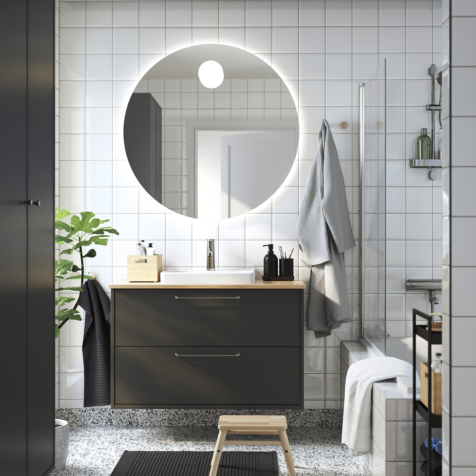 Moderne badkamer met spiegel, grijze kast, licht houten aanrechtblad, witte wastafel, grijze tegels, glazen douche en handdoeken.