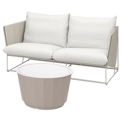 Moderne witte buitenbank met kussens en salontafel. Strak metalen frame, pluche kussens, ronde bijzettafel.