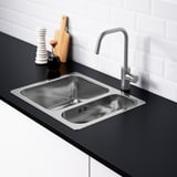 Moderne spoelbak met dubbele wastafel met kraan, zwart aanrechtblad, witte achterwand en waterafscheider.