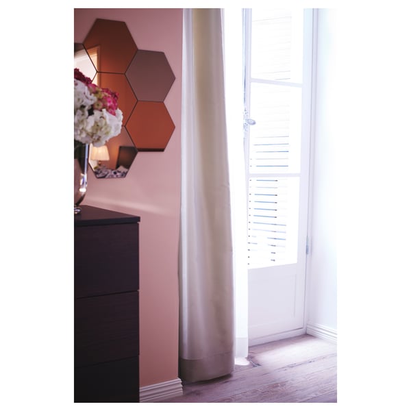 Zeshoekige oranje spiegels op roze muur dichtbij venster met wit gordijn.
