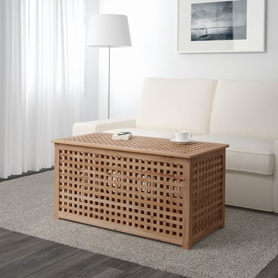Houten roostersalontafel met opbergruimte zit in de buurt van een witte bank. Het HOLds een mok en afstandsbediening en biedt praktische opbergruimte.