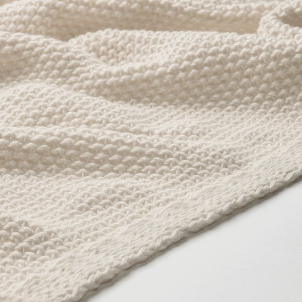 Close-up van zachte, gebroken witte gebreide deken, met textuur en vakmanschap.