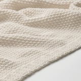 Close-up van zachte, gebroken witte gebreide deken, met textuur en vakmanschap.