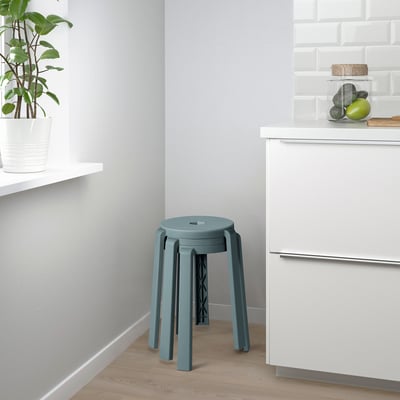 Moderne keuken met blauwe kruk, witte kasten, groene plant en fruitpot.