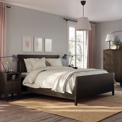 Gezellige slaapkamer met IDANÄS bed, donker hout, wit linnengoed, twee lampen, vloerkleed, roze gordijnen, kunst aan de muur, houten dressoir.