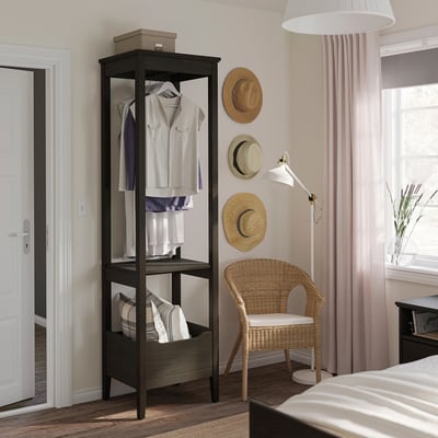 Slaapkamer met IDANÄS zwarte open kledingkast, rieten stoel, drie hoeden aan de muur en roze gordijnen.