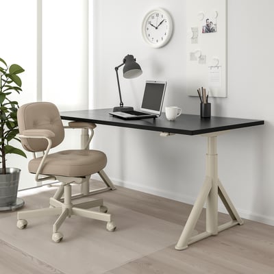 Zwart IDÅSEN verstelbaar bureau, witte voet, beige stoel, lamp, laptop, beker en whiteboard. Nette, efficiënte werkruimte voor werk en studie.