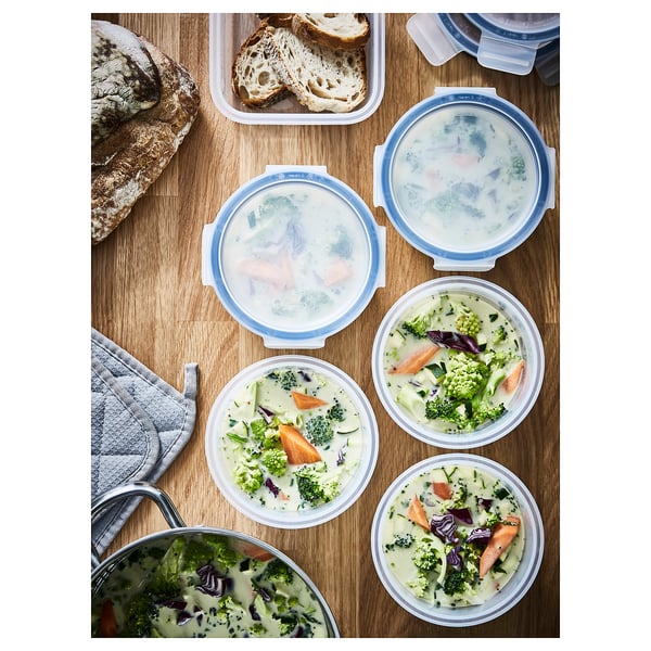 IKEA 365+ blauwe bakjes met deksel en soep en brood. Ronde, doorzichtige plastic voedselcontainers met blauwe klikdeksels gevuld met broccolisoep.
