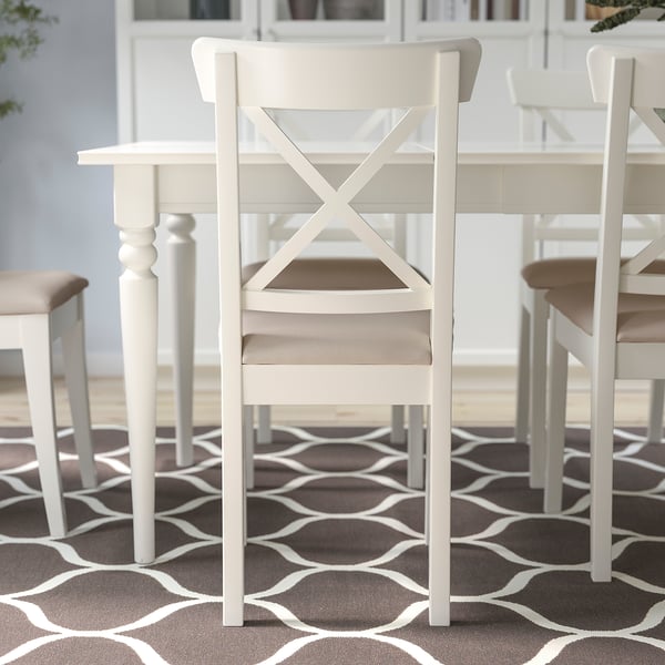Witte houten stoel met een beige gewatteerde zitting, met een gekruist rugontwerp, ideaal voor gebruik in de eetkamer.