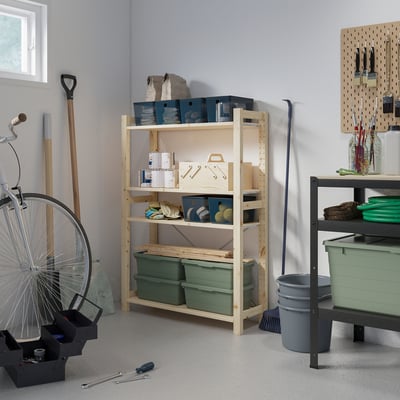 Een garage met houten IVAR planken met gereedschappen en items. De grote lichtgekleurde plank staat hoog met groene bakken en andere opgeborgen spullen.