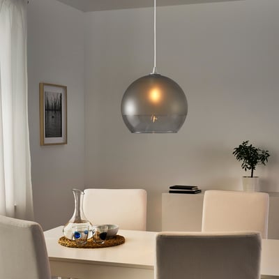 Moderne eethoek met glazen hanglamp boven witte tafel en beige stoelen, dienblad met kruik en glazen.