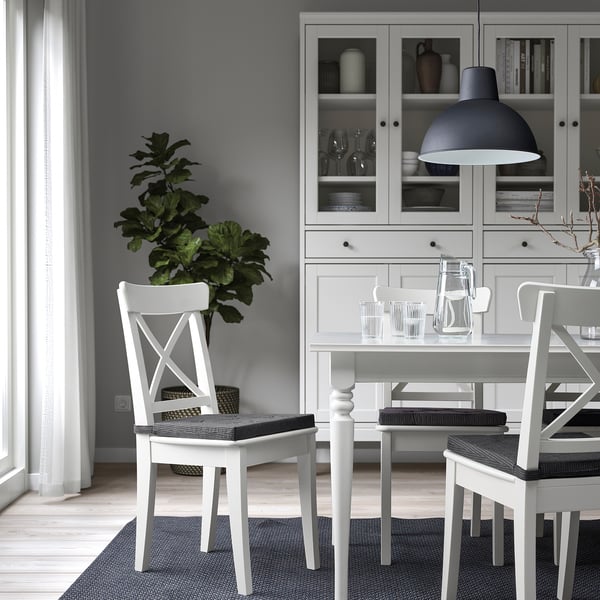 Moderne eetkamer met witte JUSTINA-stoelen, strakke tafel, hanglamp en grijze kast met glaswerk. Minimalistisch decor.