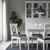Moderne eetkamer met witte JUSTINA-stoelen, strakke tafel, hanglamp en grijze kast met glaswerk. Minimalistisch decor.