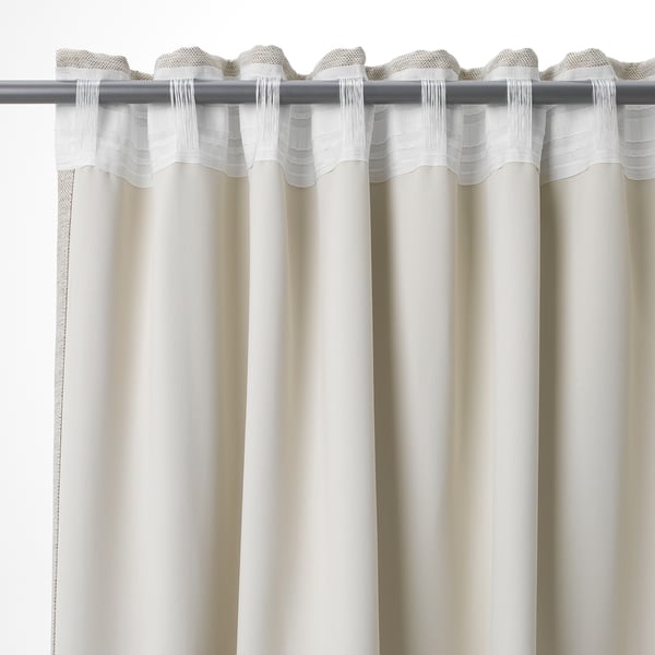 Witte gordijnen hangen met plooien, wat zorgt voor privacy en verduistering van de kamer. Lipjes en haken zichtbaar aan de bovenkant.