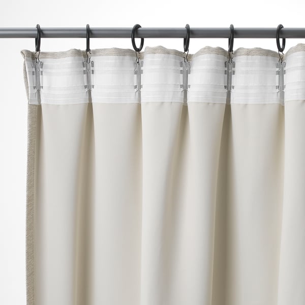 Drie beige gordijnen met geplooide bovenkanten hangen aan een metalen stang, met haken voor eenvoudige aanpassingen en privacy.