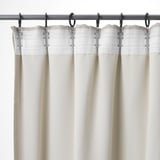 Drie beige gordijnen met geplooide bovenkanten hangen aan een metalen stang, met haken voor eenvoudige aanpassingen en privacy.