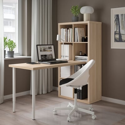 Moderne thuiskantooropstelling met licht houten KALLAX bureau en opbergruimte. Witte bureaustoel, laptop en decor. Strak en georganiseerd ontwerp.