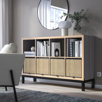 Moderne woonkamer met KALLAX rekkenkast, licht hout en zwart. Boeken en decoratie tentoonstellen. Spiegel boven, grijze stoel ernaast, lijkend op de grootte van de kamer.