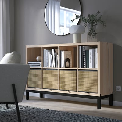 KALLAX honingraatplanken met licht hout, groenachtige planten en witte lamp; grote, lage, moderne boekenkast.