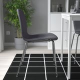 Moderne stoel met chromen poten zit op een zwart rasterkleed. Onderdeel van een minimalistische binnenomgeving.